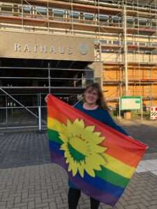 Jutta Wegner steht vor dem Neubrandenburger Rathaus und hält eine Regenbogenflagge in ihren Händen.
