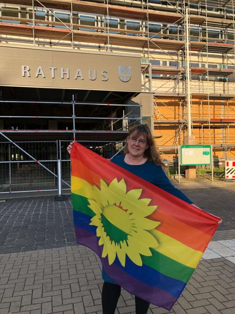 Jutta Wegner steht vor dem Neubrandenburger Rathaus und hält eine Regenbogenflagge in ihren Händen.