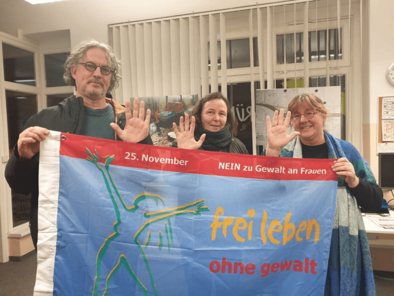 Rainer Kirchhefer, Steffi Kühn und Jutta Wegner halten gemeinsam ein Banner mit der Aufschrift "NEIN zu Gewalt an Frauen!"